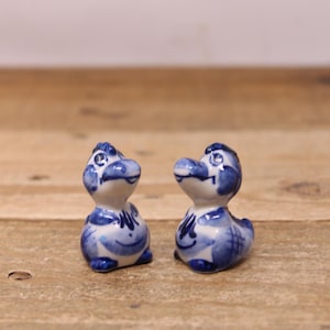May include: Two small, ceramic duck figurines. Each duck is painted with a blue and white floral pattern. The ducks are standing on a wooden surface.