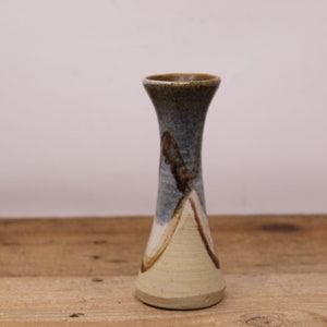 May include: A small, brown, blue, and white ceramic vase with a flared opening and a narrow base.