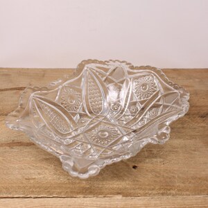 May include: A clear glass serving bowl with a scalloped edge and intricate cut glass design. The bowl is made of pressed glass and has a vintage look.