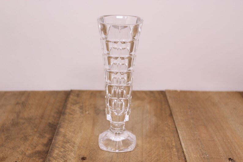 May include: A clear glass vase with a geometric pattern. The vase has a wide base and a narrow neck.