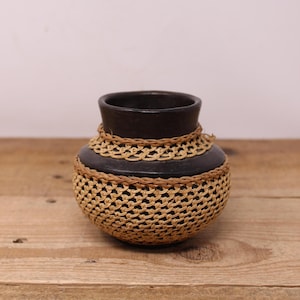 May include: A small, dark brown ceramic vase with a woven, light brown, straw-like pattern around the middle.