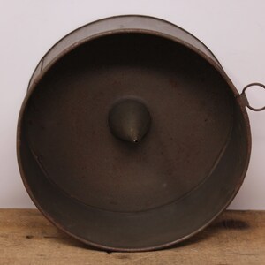 May include: A vintage metal cake tin with a removable base and a central cone. The tin is dark grey and has a ring handle.