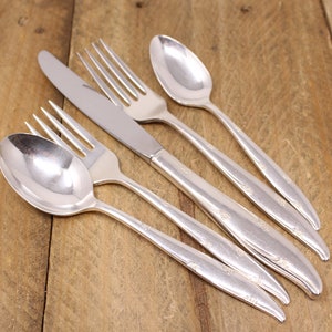 May include: A set of five silver-plated cutlery pieces, including a knife, two forks, and two spoons, arranged on a wooden surface.