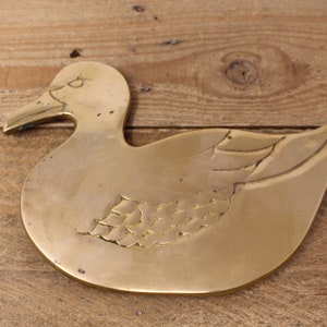 Pode incluir: Um descanso de panela de metal dourado em forma de pato. O pato tem um design detalhado de penas em suas asas.