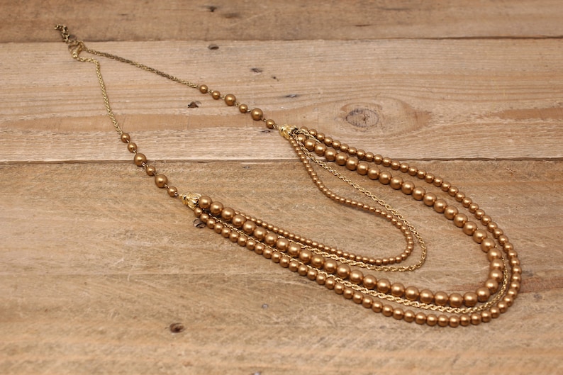 May include: A multi-strand gold necklace with brown faux pearl beads. The necklace is layered with different lengths of chain and beads.