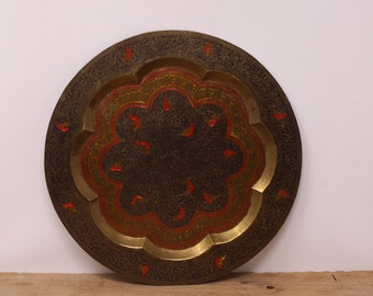May include: A round brass tray with intricate floral designs in red, gold, and black. The tray has a scalloped edge and a raised center.