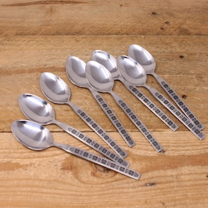 May include: A set of eight silver spoons with a decorative pattern. The spoons are arranged in a fan shape on a wooden surface.