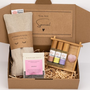 May include: A brown cardboard box filled with self-care items. The box contains a lavender eye pillow, three essential oil roller bottles, a pink heart-shaped crystal, and a packet of tea. The box has a label that says "You Are Special".