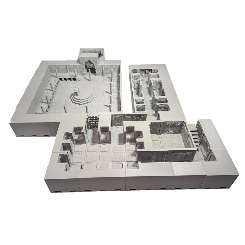 May include: A white 3D printed model of a dungeon or castle interior. The model is made up of multiple sections that can be assembled to create a complex layout. The model features a variety of rooms, corridors, and other features, including a central courtyard and a staircase.