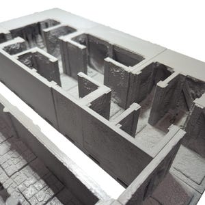 May include: A 3D printed model of a dungeon or castle interior. The model is made of gray plastic and features a series of rooms and corridors. The model is designed for use in tabletop role-playing games.