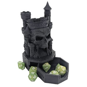 May include: Black skull-shaped dice tower with a castle design. The tower has a removable tray with compartments for dice. Green dice with white numbers are scattered around the tower.