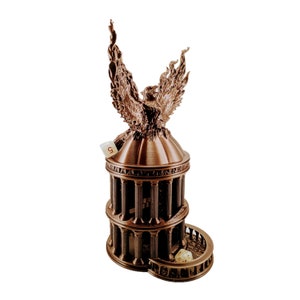 May include: A bronze tabletop dice tower with a phoenix on top. The tower has three levels and a circular base. A white die is visible in the base.