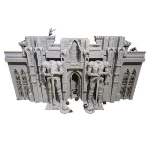 May include: A gray miniature castle model with two headless knight statues holding swords. The castle has arched windows, a central doorway, and decorative gargoyles. The model is designed for tabletop gaming.