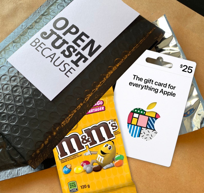 Może przedstawiać: Czarno-biała karta podarunkowa z tekstem "The gift card for everything Apple" i kolorowym wzorem jabłka. Karta podarunkowa jest warta 25 $. Karta podarunkowa leży na brązowej kopercie bąbelkowej z tekstem "OPEN JUST BECAUSE" na białym kartonie.