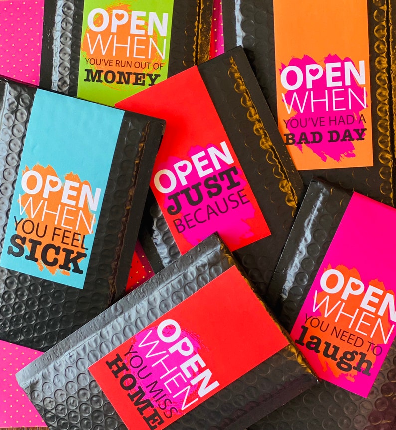 Może przedstawiać: Zbi&oacute;r kolorowych kopert z tekstem "Open When" po kt&oacute;rym następują r&oacute;żne zwroty, takie jak "You've Run Out of Money", "You've Had a Bad Day", "You Feel Sick", "Just Because", "You Miss Home" i "You Need to Laugh".