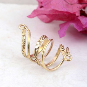 Può includere: Un anello a spirale color oro con motivi floreali e a foglie. L'anello ha un design unico con più fasce e una vestibilità aperta e regolabile. L'anello è in metallo ed è probabilmente un accessorio di moda.