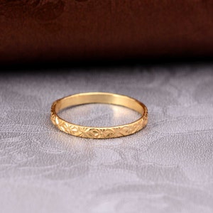May include: A gold ring with a detailed floral pattern. The ring is thin and appears to be made of metal. The ring is displayed on a textured, light grey surface.