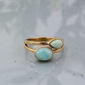 Può includere: Un anello color oro con due pietre preziose azzurre. Una gemma è ovale, l'altra a forma di goccia. L'anello ha un design a gambo diviso, con le gemme incastonate sulla parte superiore.