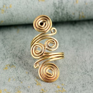 May include: A gold-coloured ring with a distinctive spiral design. The ring has several swirling coils of metal, creating an eye-catching and artistic appearance. The ring is made of a shiny, metallic material.