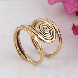 Può includere: Un anello color oro con una texture martellata e un design a spirale. L'anello presenta una fascia regolabile e un elemento a spirale prominente, creando un look unico e artistico. L'anello è realizzato in materiale metallico lucido.