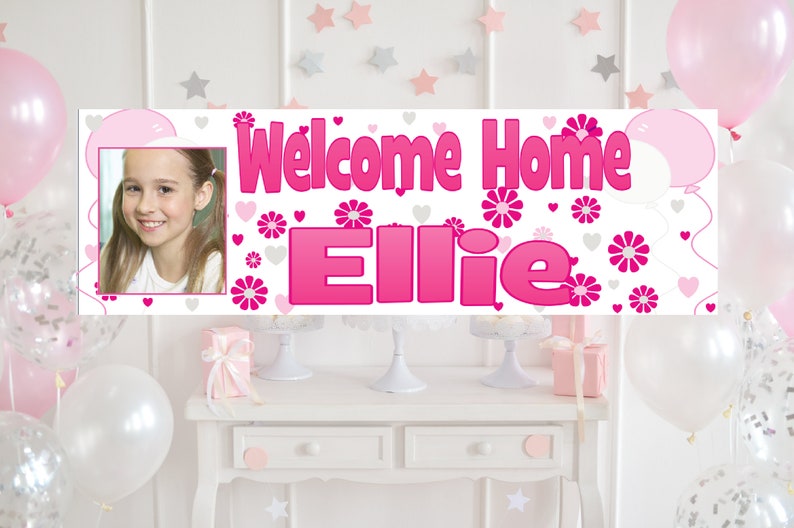 Puede incluir: Una pancarta de bienvenida a casa rosa y blanca con una foto de una ni&ntilde;a y el nombre "Ellie" en letras rosas. La pancarta est&aacute; decorada con corazones y flores rosas.