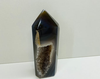 May include: A polished agate crystal point with a dark brown and grey exterior. The crystal has a hollowed-out section with a sparkling, crystal-filled interior. The top of the crystal is a flat, angled surface.