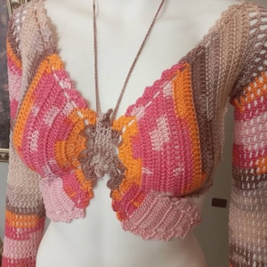 May include: A crocheted top with long sleeves in a rainbow colour pattern of pink, orange, and brown. The top has a V-neck and a tie at the front.