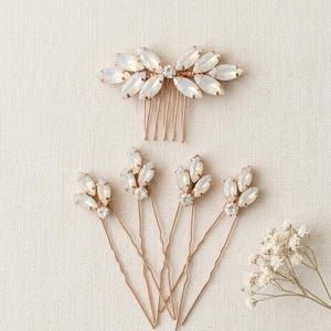 May include: A rose gold hair comb and four matching hair pins, each featuring marquise-cut opalescent stones arranged in leaf-like clusters with small clear round crystals at the centre of the pin designs and the comb base.