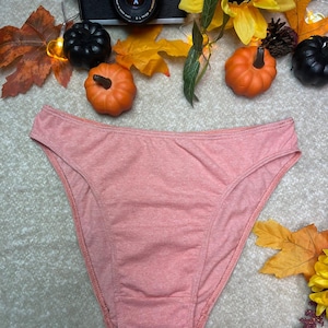 May include: A peach-colored cotton thong underwear with a high leg cut. The underwear is photographed on a white surface with fall-themed decorations.