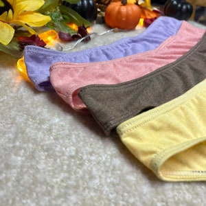 May include: Four pairs of underwear in different colors: purple, pink, brown, and yellow. The underwear is made of a soft, stretchy fabric.