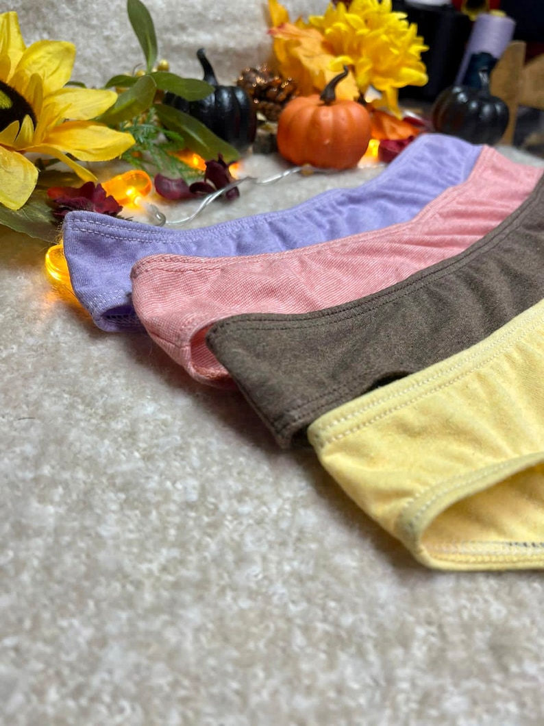 May include: Four pairs of underwear in different colors: purple, pink, brown, and yellow. The underwear is made of a soft, stretchy fabric.