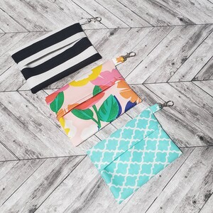 May include: Three fabric pouches with zipper closures and attached key rings. The pouches are made of different patterned fabrics: black and white stripes, pink with floral print, and turquoise with a geometric pattern.