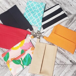 May include: Seven different fabric pouches with various patterns and colors. The pouches are made of different fabrics, including black, red, orange, beige, white, and blue. The pouches are all lined up in a circle on a wooden surface.