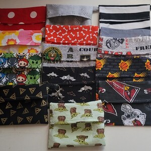 May include: A collection of 11 fabric pouches with various designs and patterns. The pouches are made of cotton fabric and have a drawstring closure. The designs include polka dots, bone patterns, a superhero theme, a sports team logo, and a baby Yoda character.