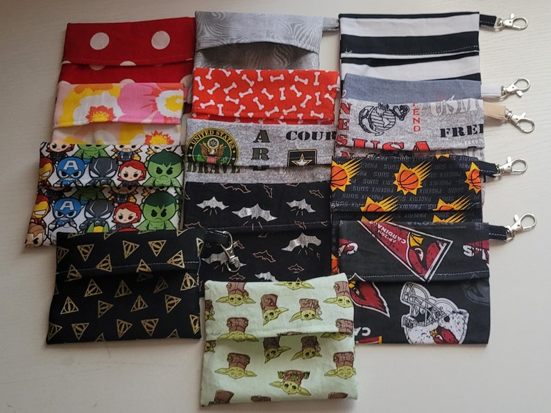 May include: A collection of 11 fabric pouches with various designs and patterns. The pouches are made of cotton fabric and have a drawstring closure. The designs include polka dots, bone patterns, a superhero theme, a sports team logo, and a baby Yoda character.
