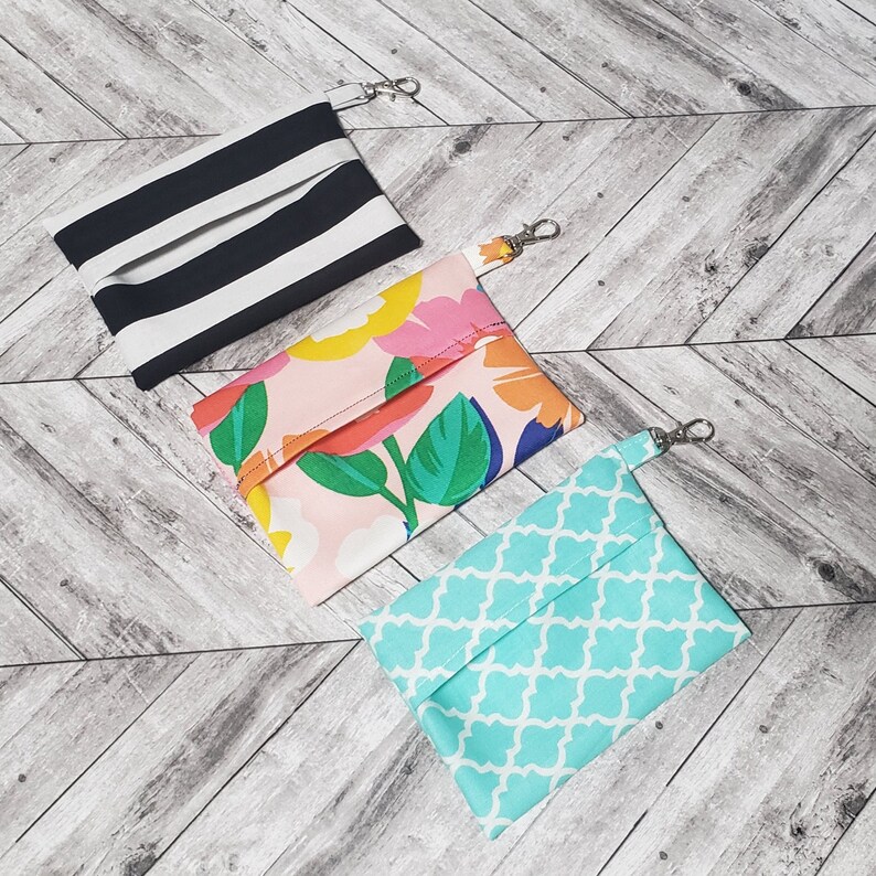 May include: Three fabric pouches with zipper closures and attached key rings. The pouches are made of different patterned fabrics: black and white stripes, pink with floral print, and turquoise with a geometric pattern.