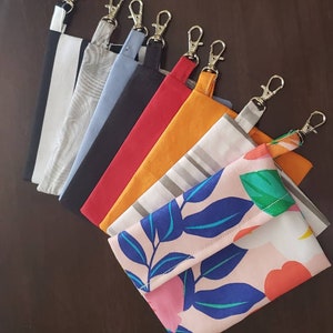 May include: A set of nine fabric pouches with zipper closures and metal key rings. The pouches are in various colors and patterns, including black, red, orange, gray, and a floral print.