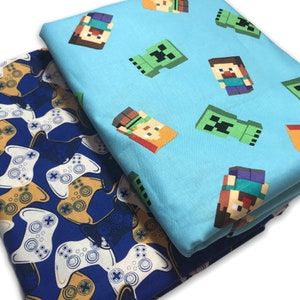 May include: Two fabric panels, one blue with a repeating pattern of Minecraft characters, and one navy blue with a repeating pattern of video game controllers.