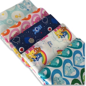 May include: Five different fabric panels featuring Care Bears characters. The panels are stacked on top of each other, with the top panel showing a blue and white pattern with Care Bears in hearts. The second panel shows a white background with a rainbow and Care Bears. The third panel shows a blue background with Care Bears and stars. The fourth panel shows a pink background with Care Bears and rainbows. The bottom panel shows a light blue background with Care Bears and stars.