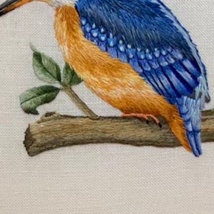 May include: A detailed embroidery of a blue and orange kingfisher perched on a branch. The bird's feathers are meticulously stitched with fine detail, creating a realistic depiction.
