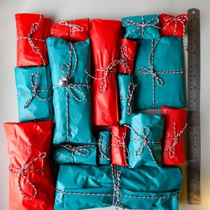 May include: A collection of wrapped gifts in red and blue paper with white string and bows. Some of the gifts have a silver bell attached.