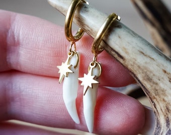 Puede incluir: Aretes de aro dorados con un dije de diente blanco y un colgante de estrella dorada.