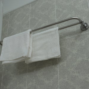 Puede incluir: Dos toallas blancas colgadas en una barra de toallas doble de plata montada en una pared de azulejos.
