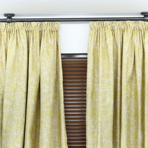 Puede incluir: Un par de cortinas de color amarillo con estampado y una barra de cortina negra. Las cortinas están colgadas en una pared blanca.