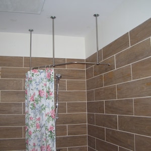 May include: A white shower curtain with pink and green floral print hangs from a curved shower rod attached to the ceiling. The shower rod is made of chrome and is attached to the ceiling with four chrome brackets.