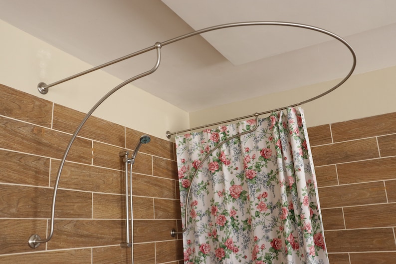 May include: A curved shower curtain rod with a floral patterned shower curtain. The rod is made of silver metal and is mounted to the ceiling and wall. The shower curtain is white with pink and green flowers.