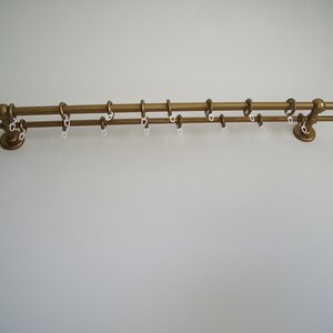 May include: A gold double curtain rod with white plastic rings. The rod is mounted on a white wall.