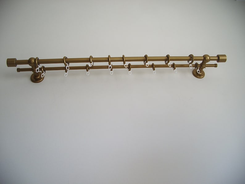 May include: A gold double curtain rod with white plastic rings. The rod is mounted on a white wall.