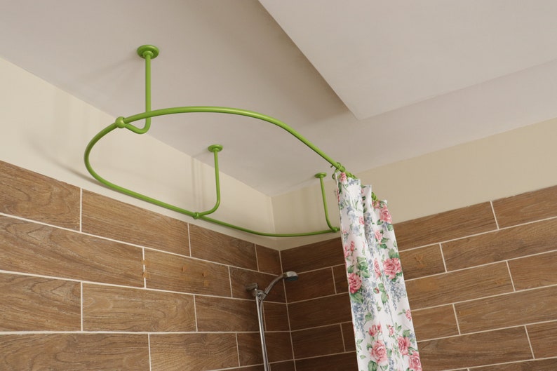 May include: A green metal shower curtain rod is installed in a corner of a bathroom. The rod is curved and has a white shower curtain with a floral pattern hanging from it.