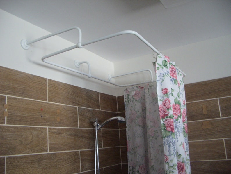 Puede incluir: Barra de cortina de ducha blanca con dos barras, montada en el techo. La barra sostiene una cortina de ducha blanca con un patr&oacute;n floral en rosa, verde y azul.